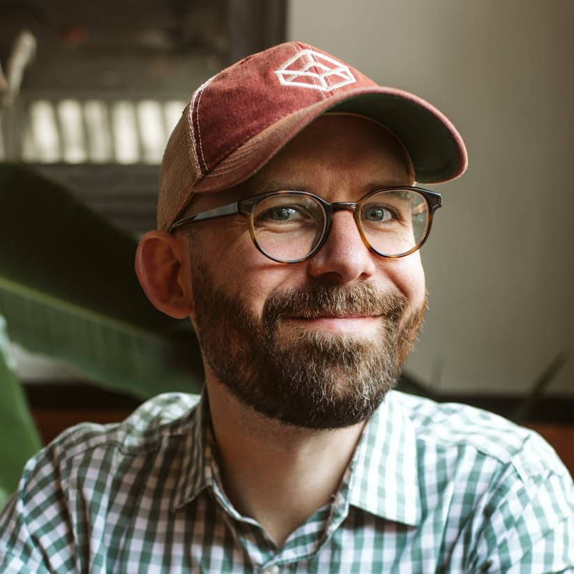 Me, Josh Collinsworth, an average middle-aged white guy in a patterned button-up, with a beard, glasses, and a CodePen trucker hat.
